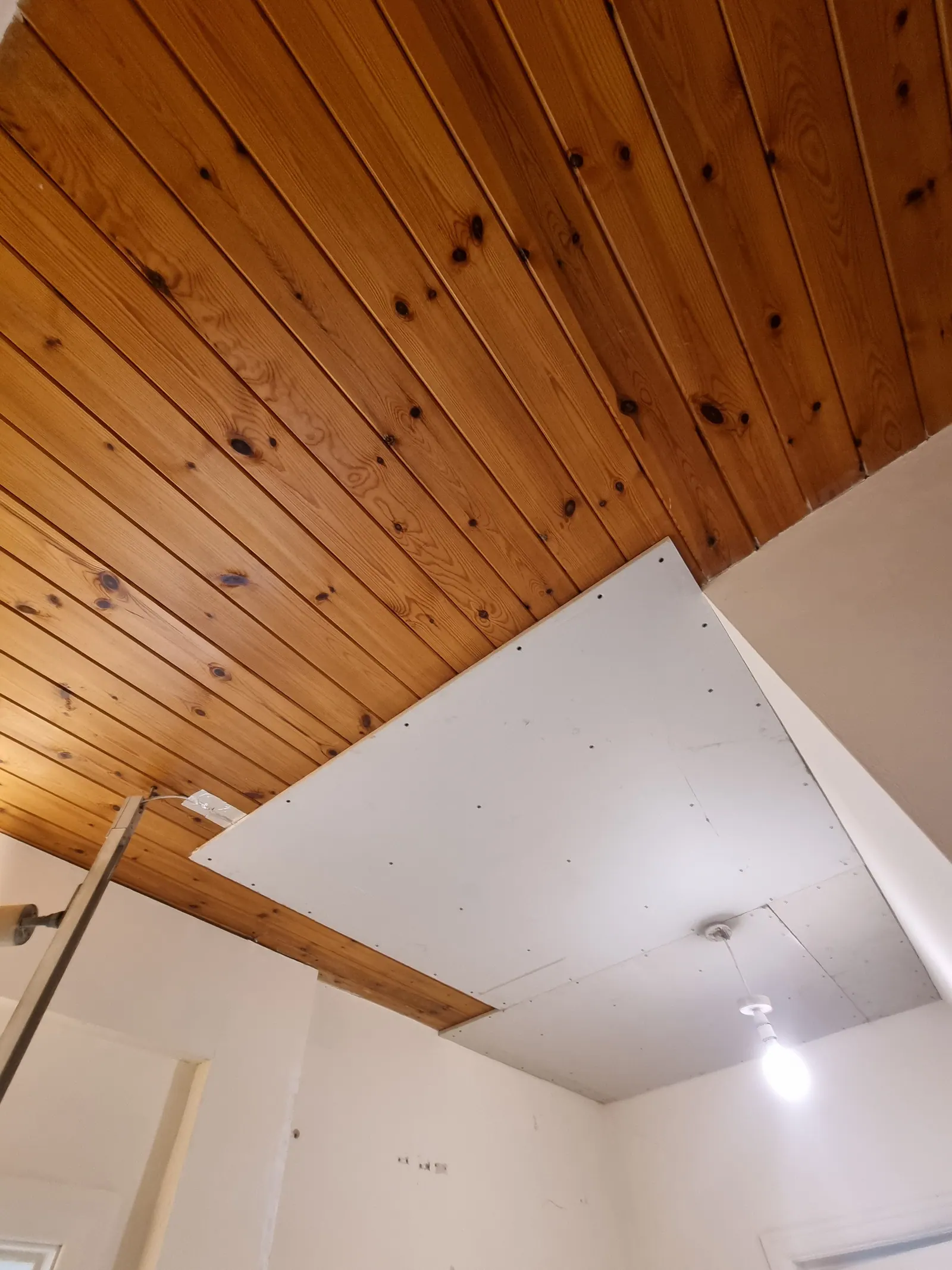 Plasterboard being fitted to a timber-clad ceiling