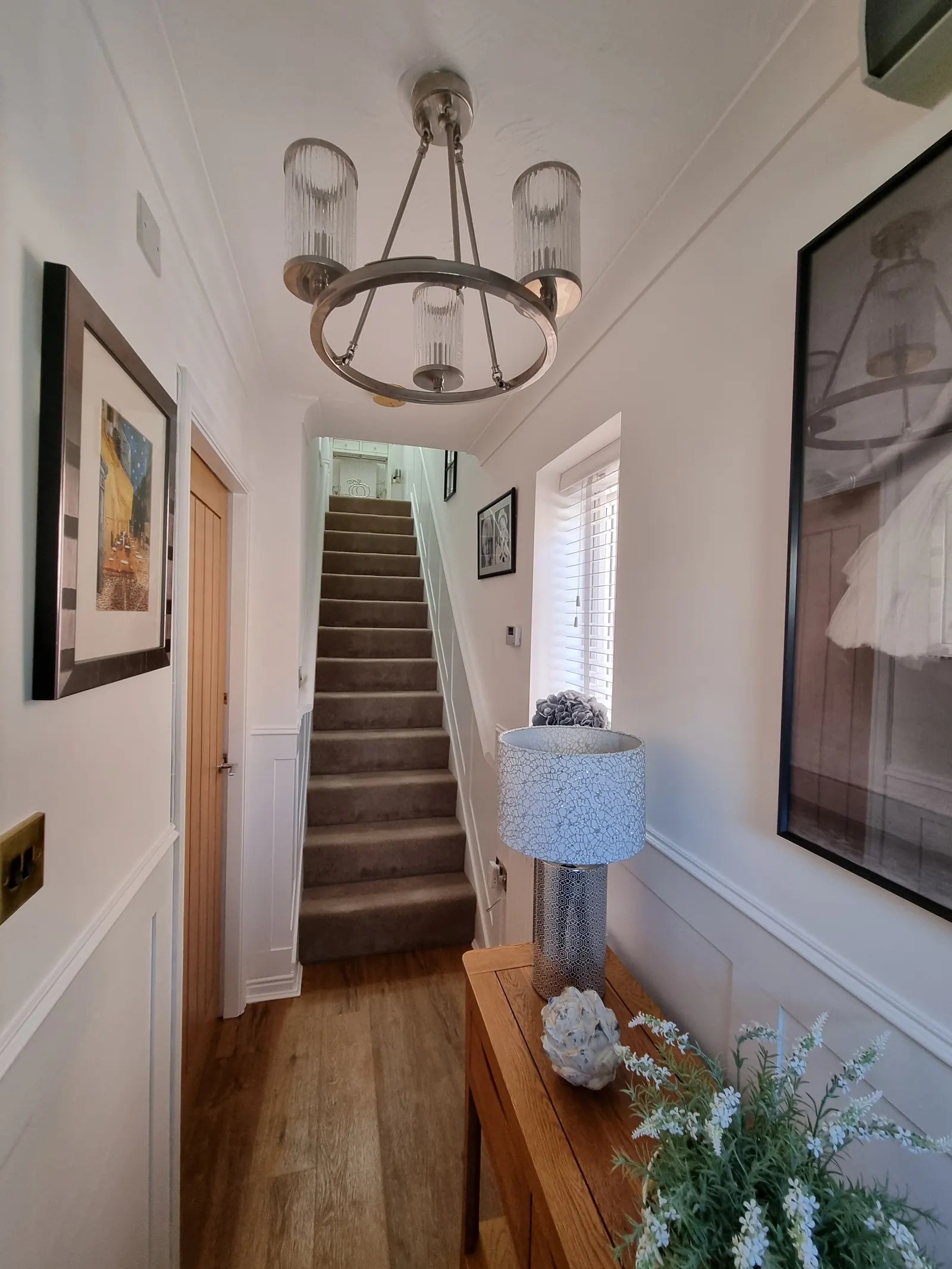 Hallway with white wall panelling, a pendant light and stairs