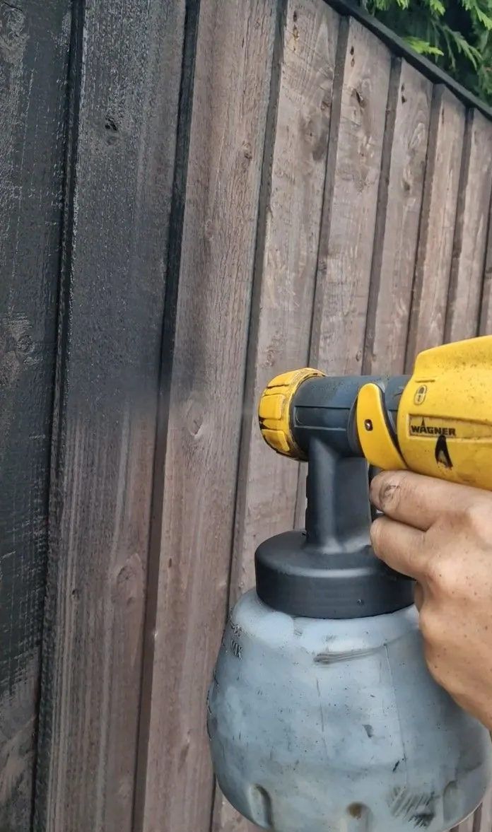 Fence panel being painted dark with a paint sprayer