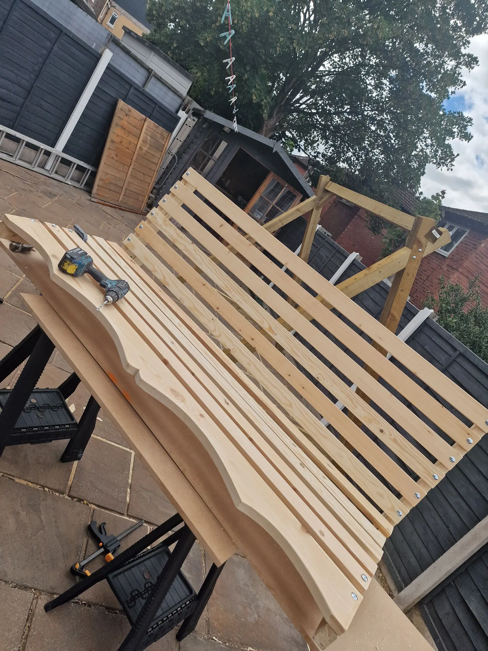 Timber garden bench being assembled, with a drill resting on the slats