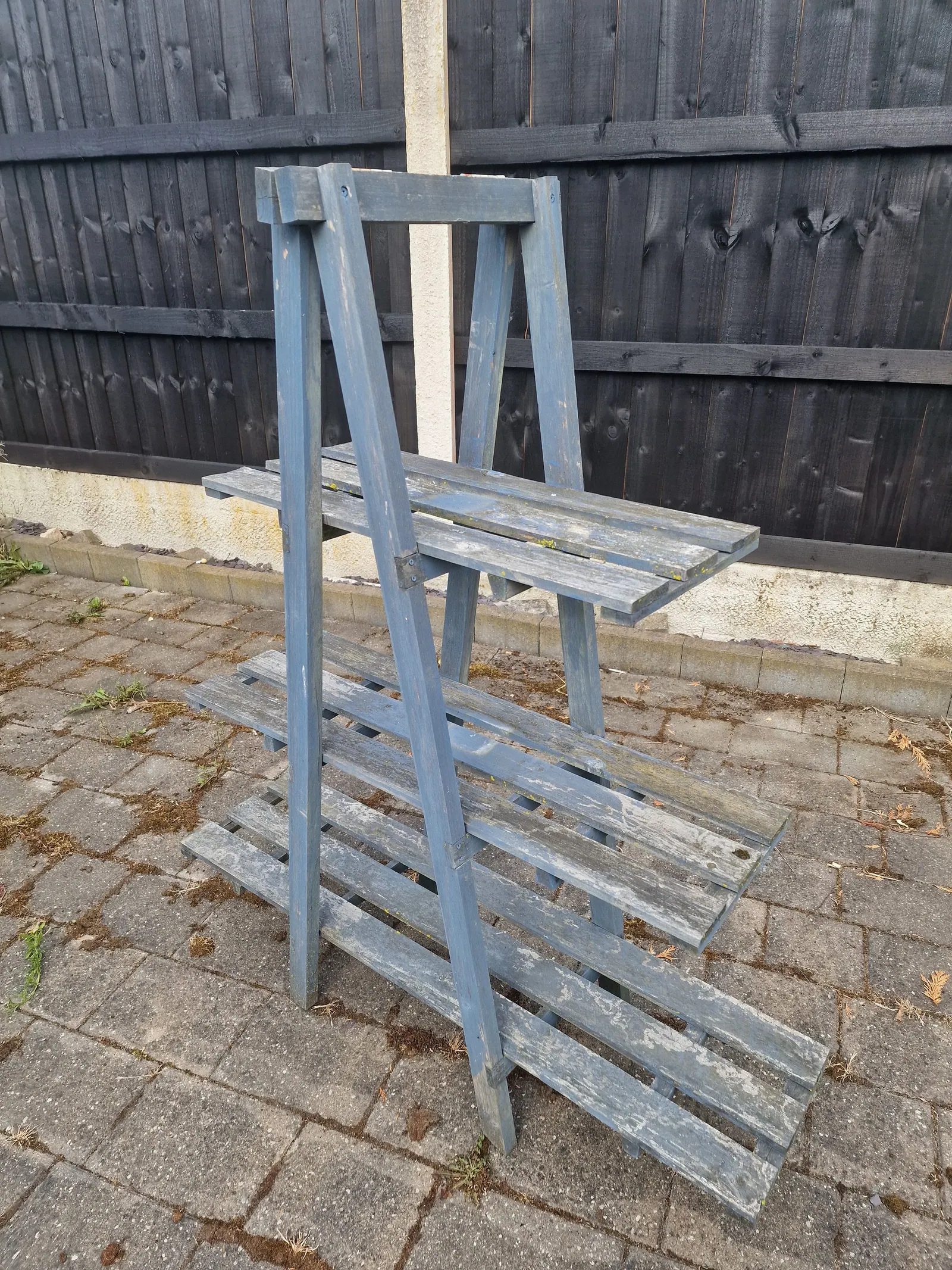 Weathered grey wooden plant stand in front of a dark fence