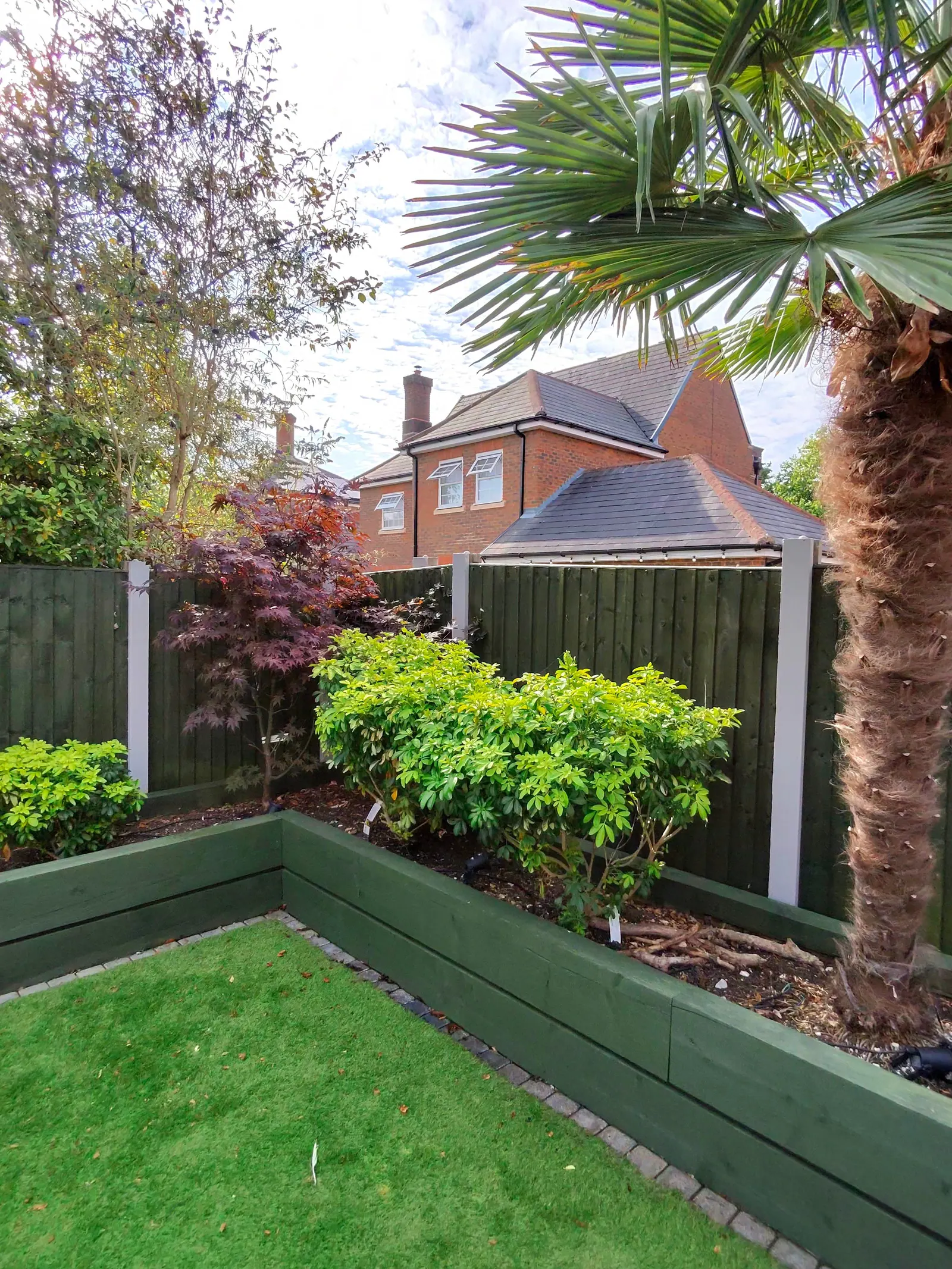 Green painted fence and sleeper raised beds around a lawn
