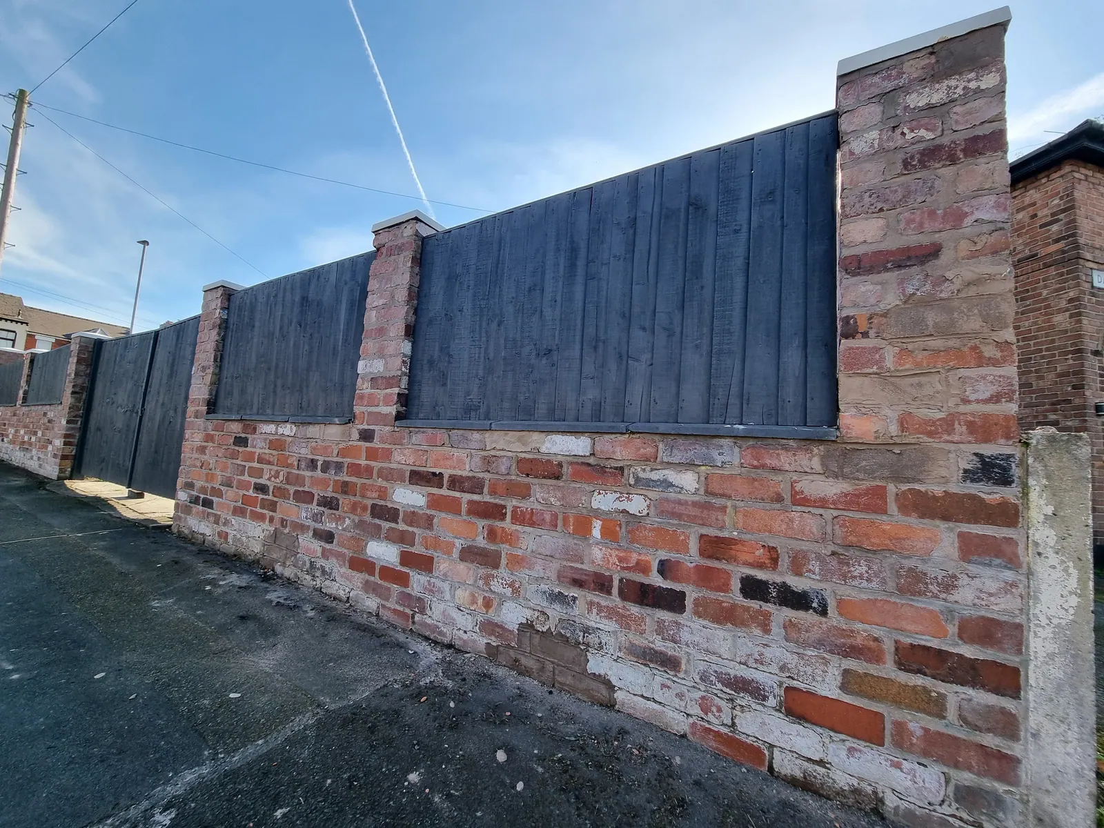 Dark painted fence panels set between brick pillars on a boundary wall