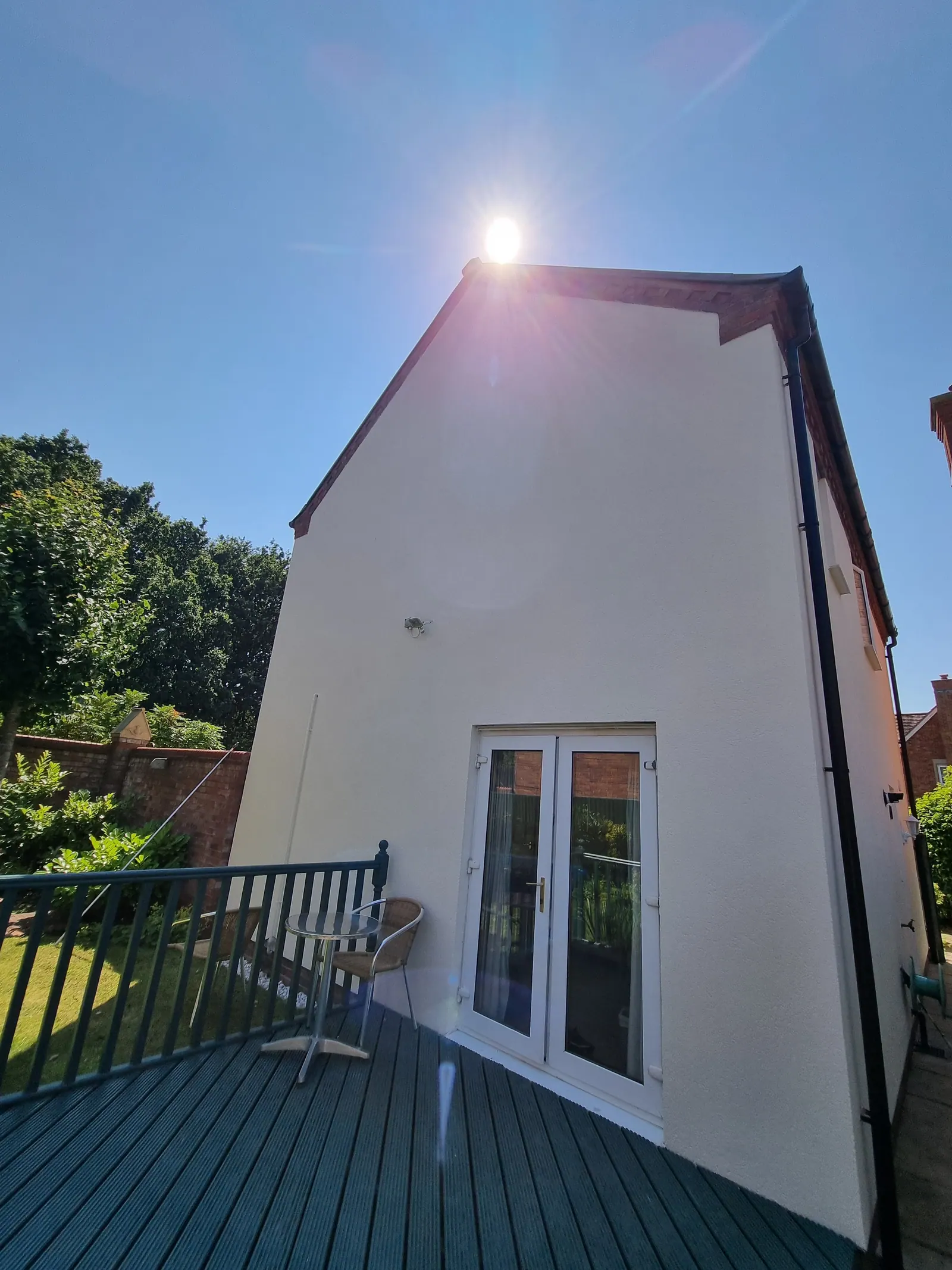 White painted gable wall with French doors above green painted decking