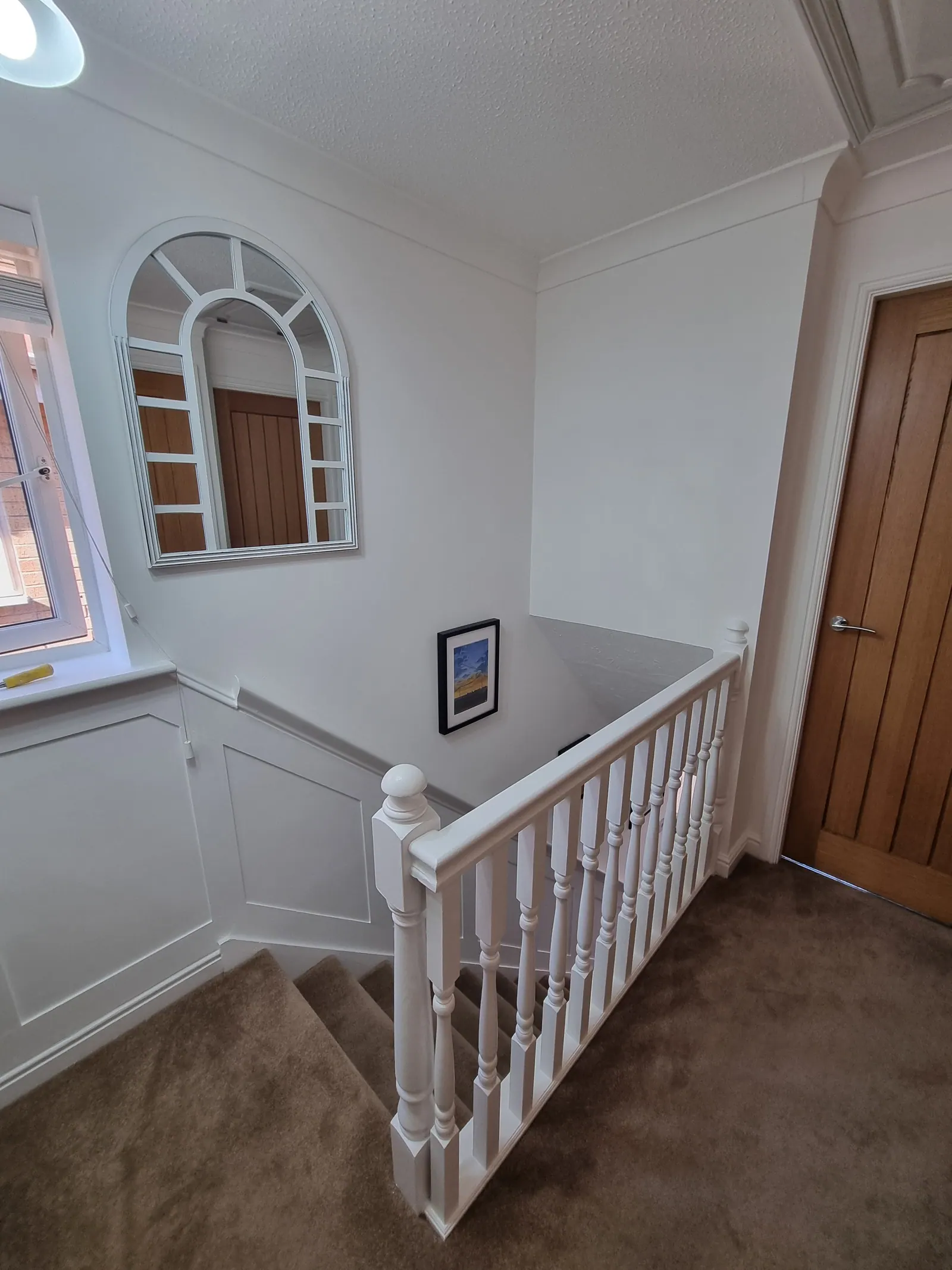 Landing with white wall panelling, a white balustrade and oak doors