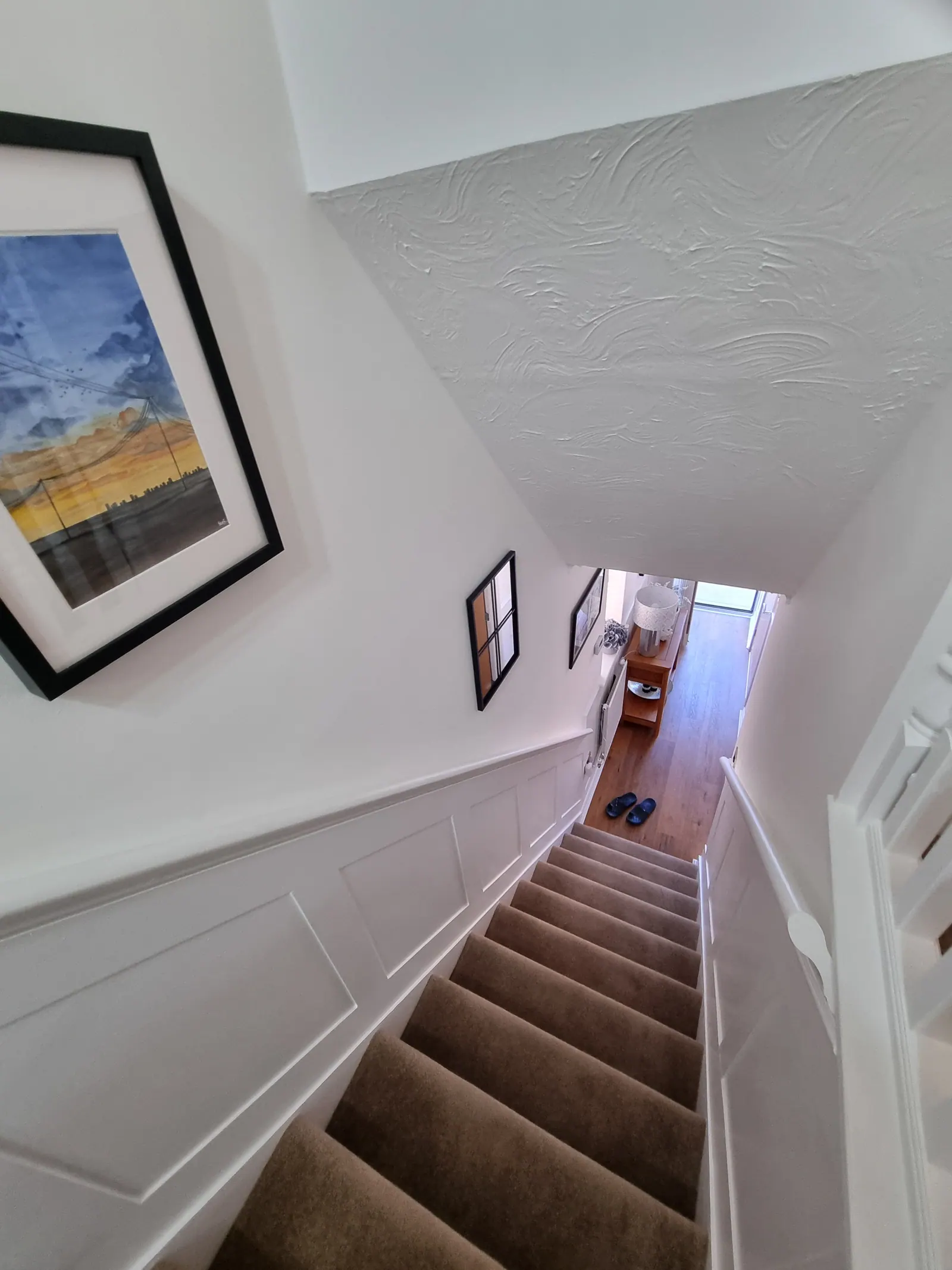 Staircase with white wall panelling and a framed print