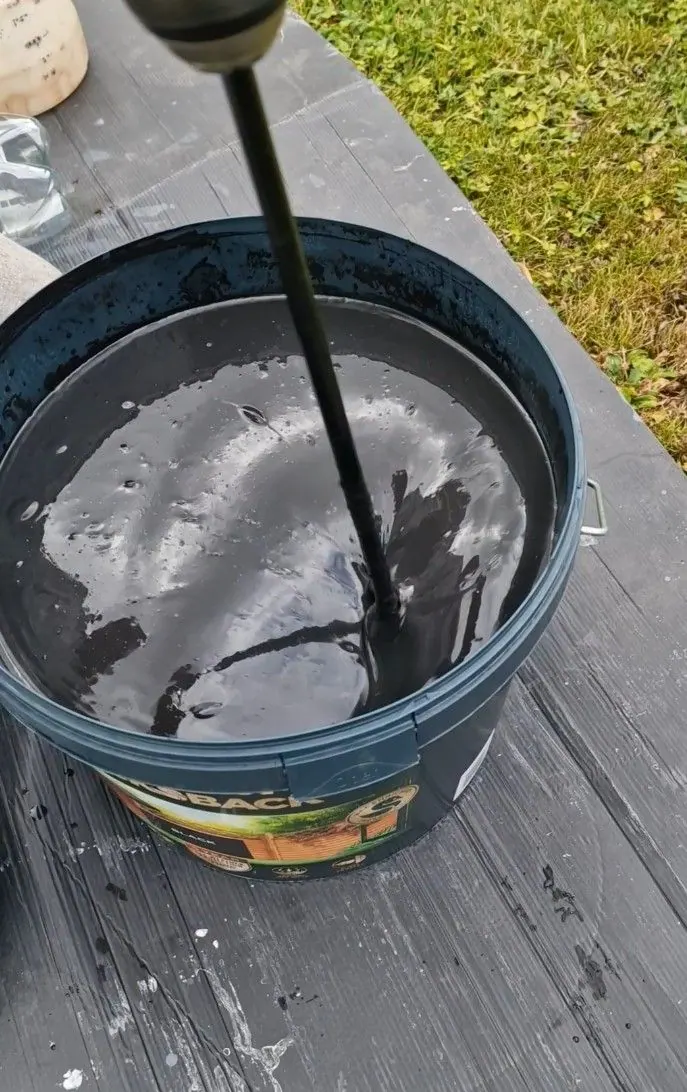 Dark fence paint being mixed in a tub