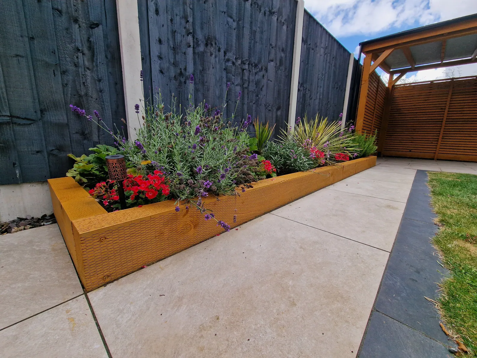 Timber raised flower bed planted with flowers beside a dark fence